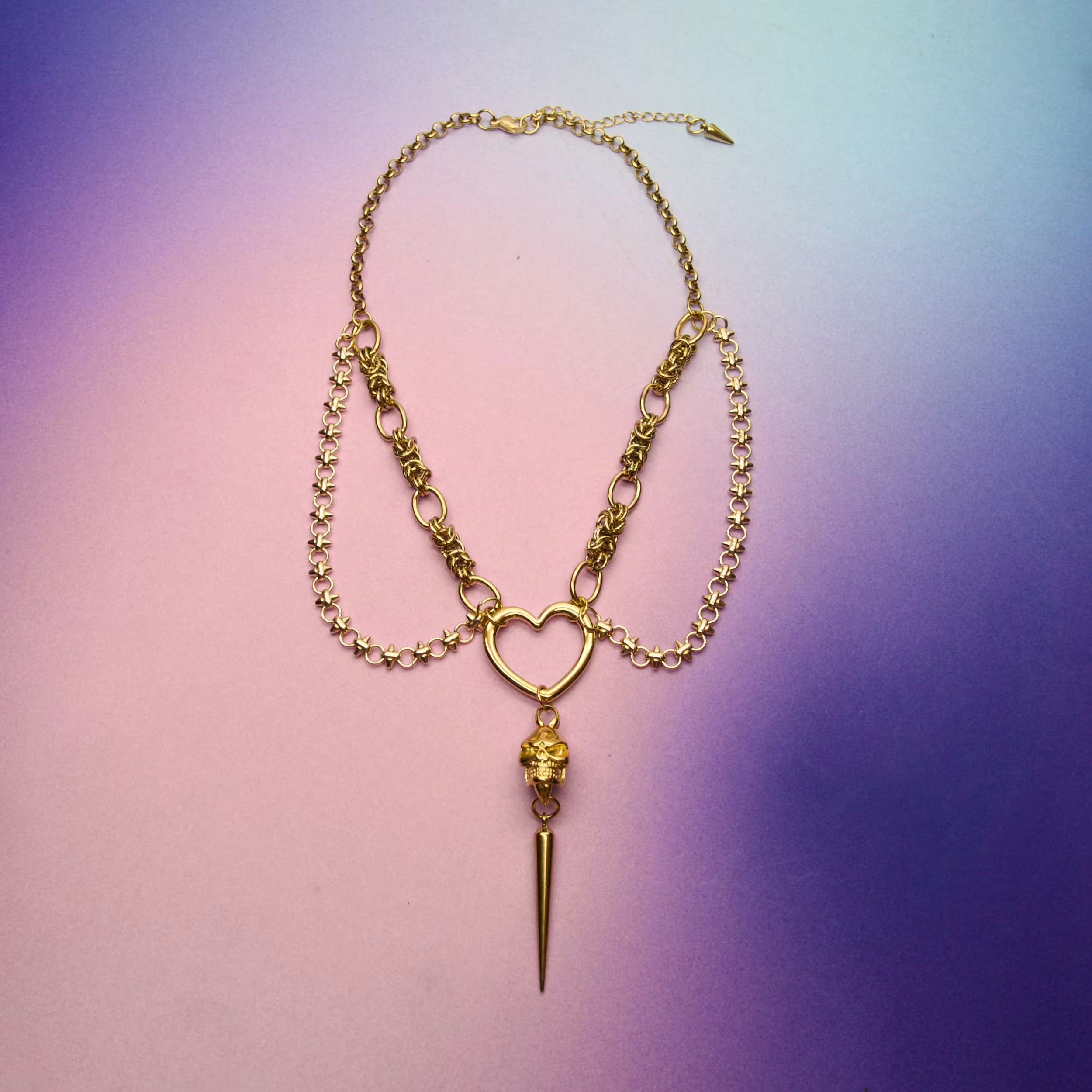 Layered gold statement chain necklace with heart link and 18k gold plated spike charm laid flat for product display.