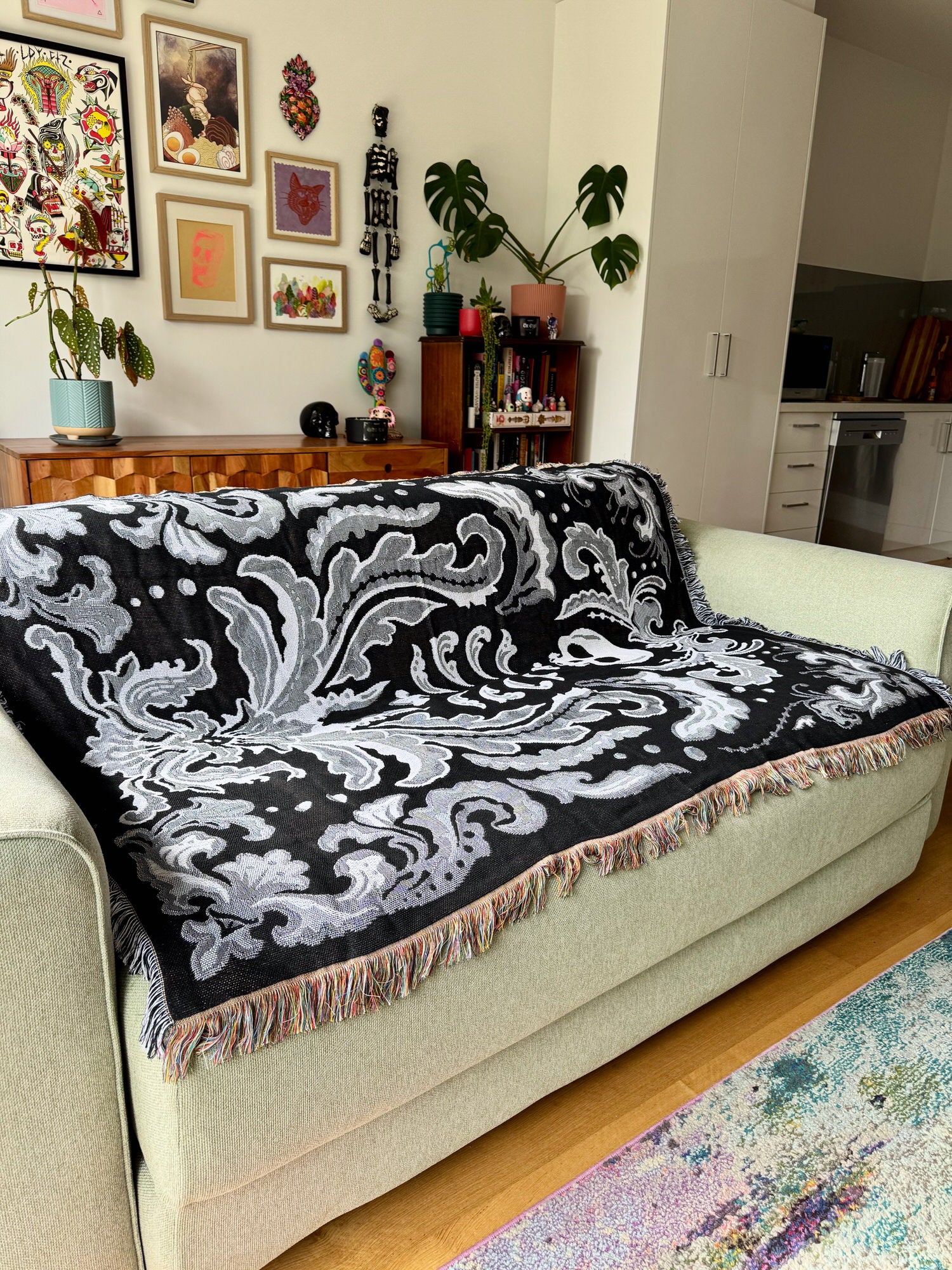 Decorative black and white patterned throw blanket on a sage sofa in a living room.