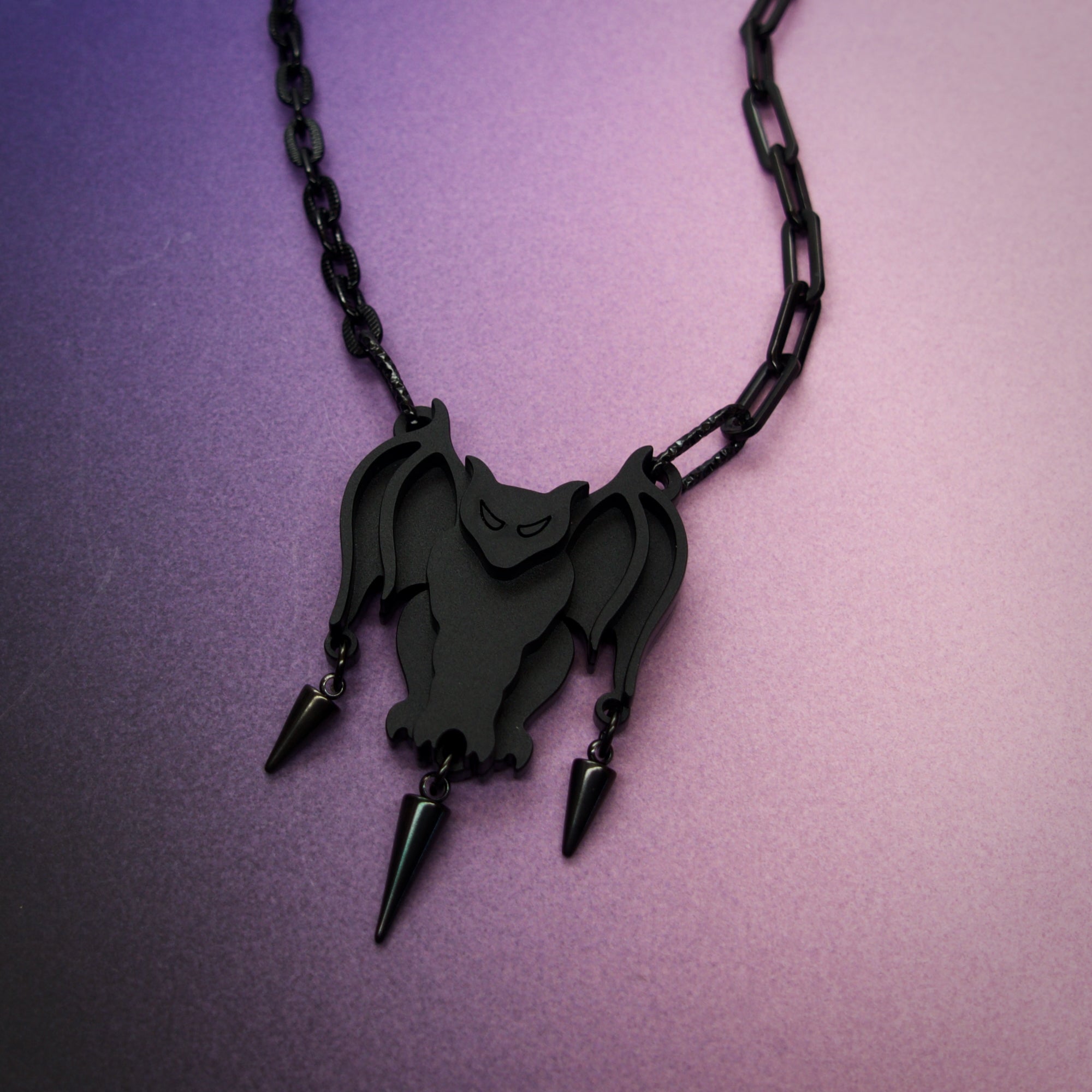 Black bat-shaped pendant necklace on a black chain against a purple background