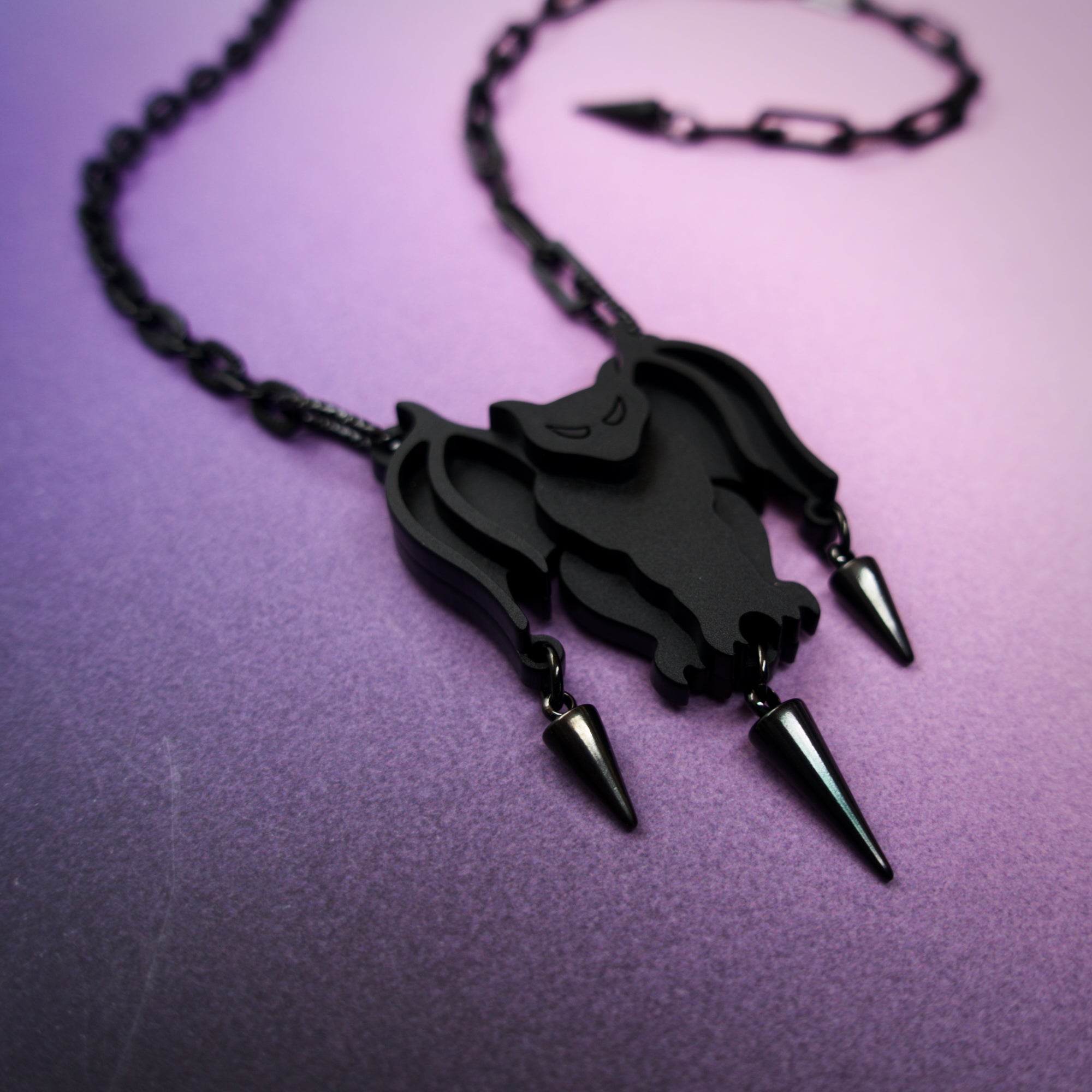 Black bat-shaped pendant necklace with spikes on a purple background