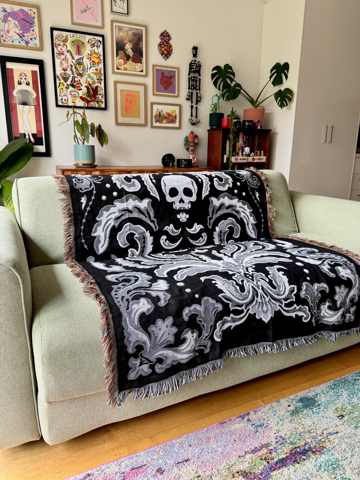 Decorative black and white skull-patterned throw blanket on a light green sofa in a living room.