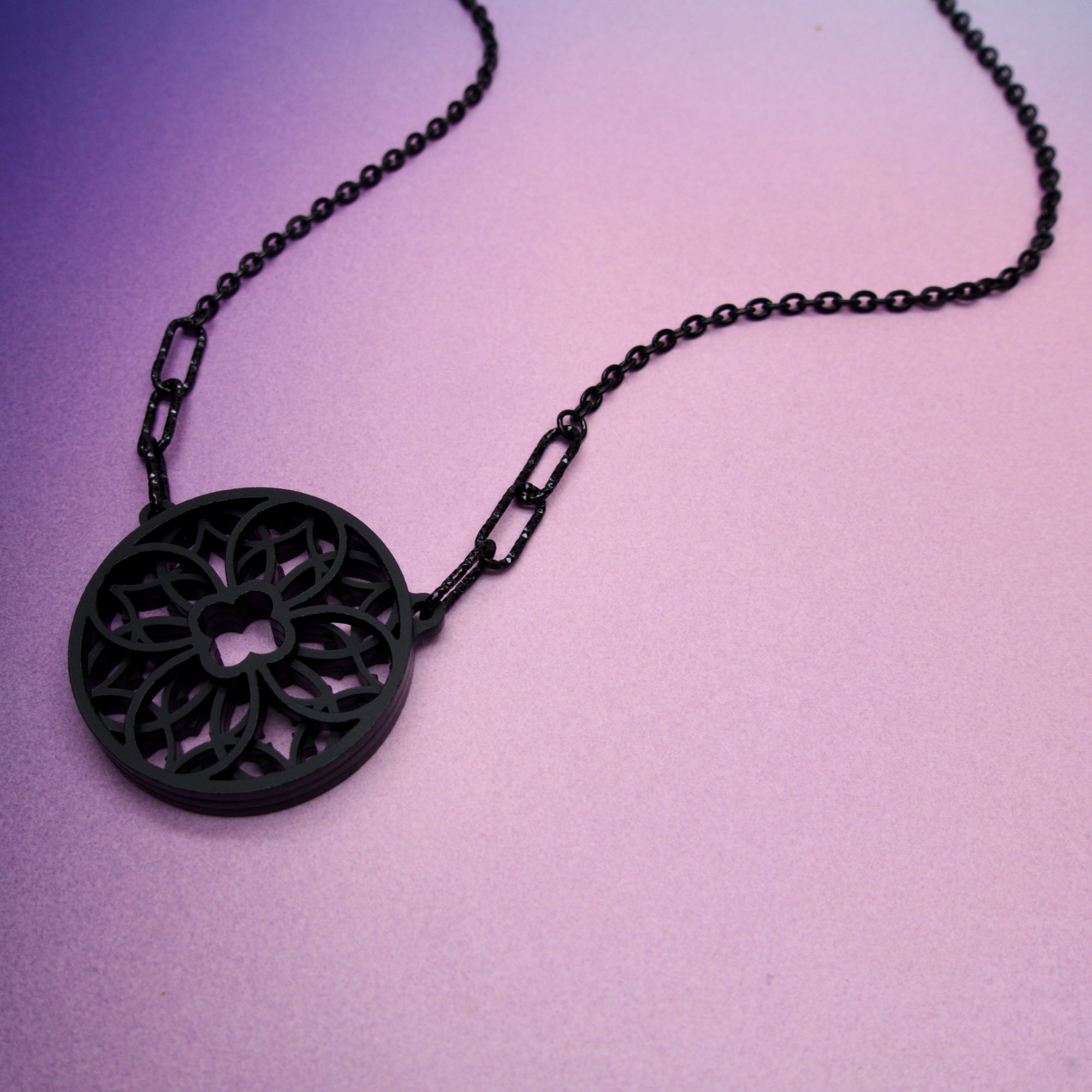 Black necklace with decorative pendant on purple background